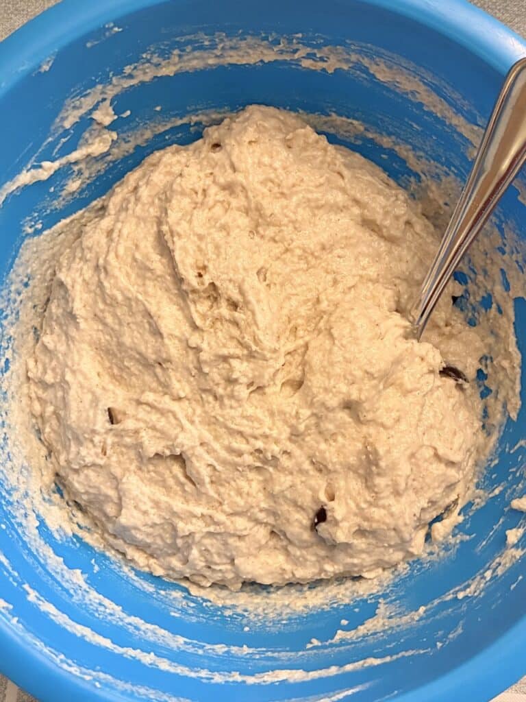 Thick gluten-free oat flour muffin batter with chocolate chips in a blue plastic mixing bowl with a stainless steel spoon.