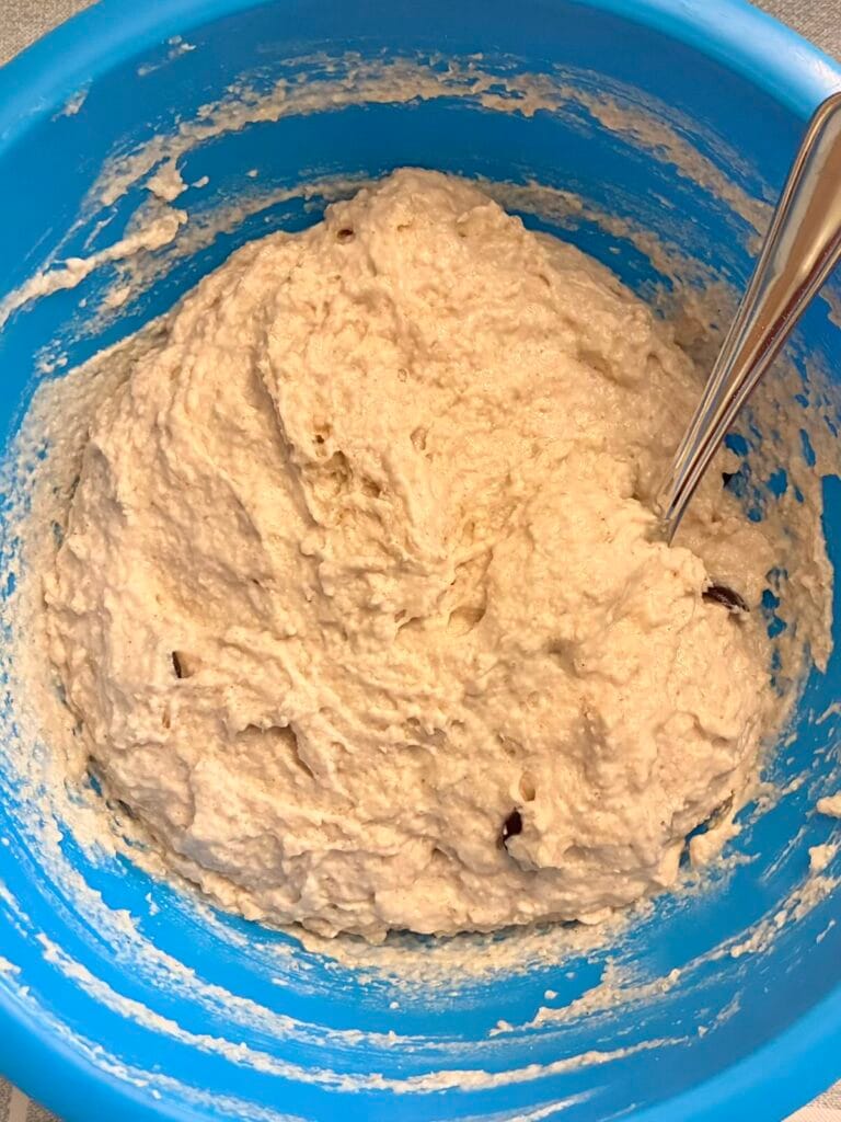 Eggless Oat Flour Chocolate Chip Muffins (No Vinegar) 4 Thick gluten-free oat flour muffin batter with chocolate chips in a blue plastic mixing bowl with a stainless steel spoon.