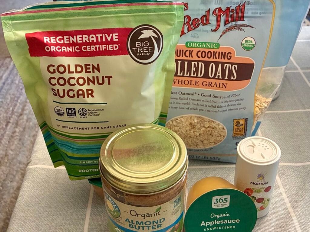 An ingredient flatlay showing quick-cooking oats, creamy almond butter, salt, and a package of Big Tree Farms Golden Coconut Sugar on a kitchen counter. 