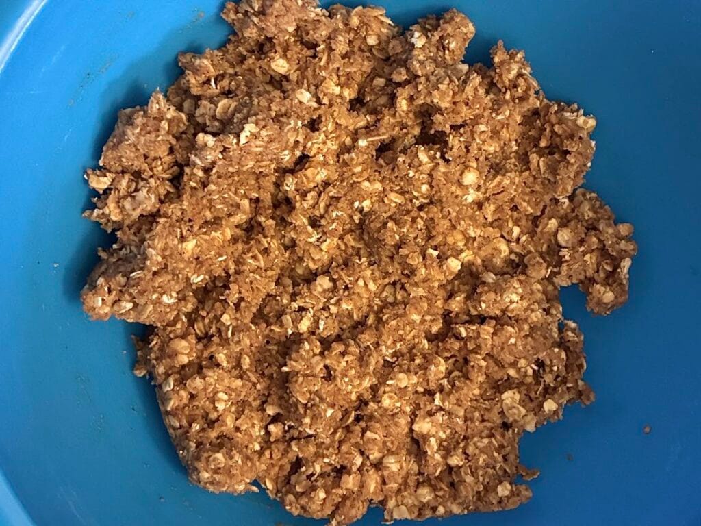 Thick and uniform eggless apple oatmeal cookie dough resting in a large mixing bowl to absorb liquid ingredients.