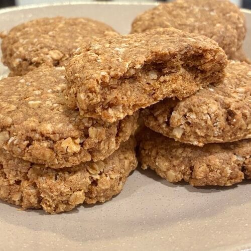 A horizontal landscape shot of fresh soft-baked eggless apple oatmeal cookies stacked in rows, featuring one cookie split in half to show the moist and chewy texture inside.