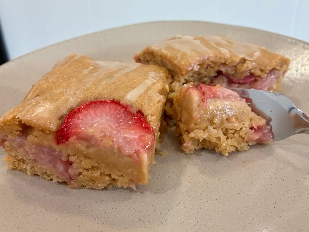 One-Bowl Strawberry Applesauce Snack Cake 5 Close up view of a fork cutting into a slice of strawberry applesauce snack cake served on a matte stoneware plate.