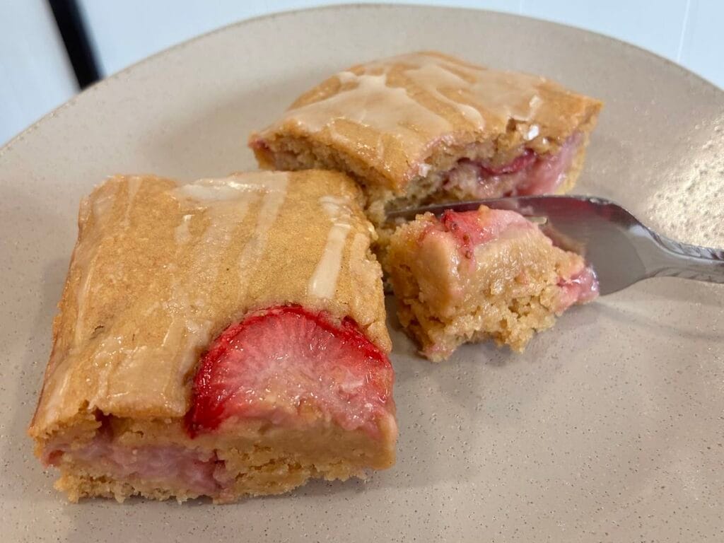 One-Bowl Strawberry Applesauce Snack Cake 4 A slice of glazed strawberry snack cake on a matte stoneware plate with a fork cutting into the side.