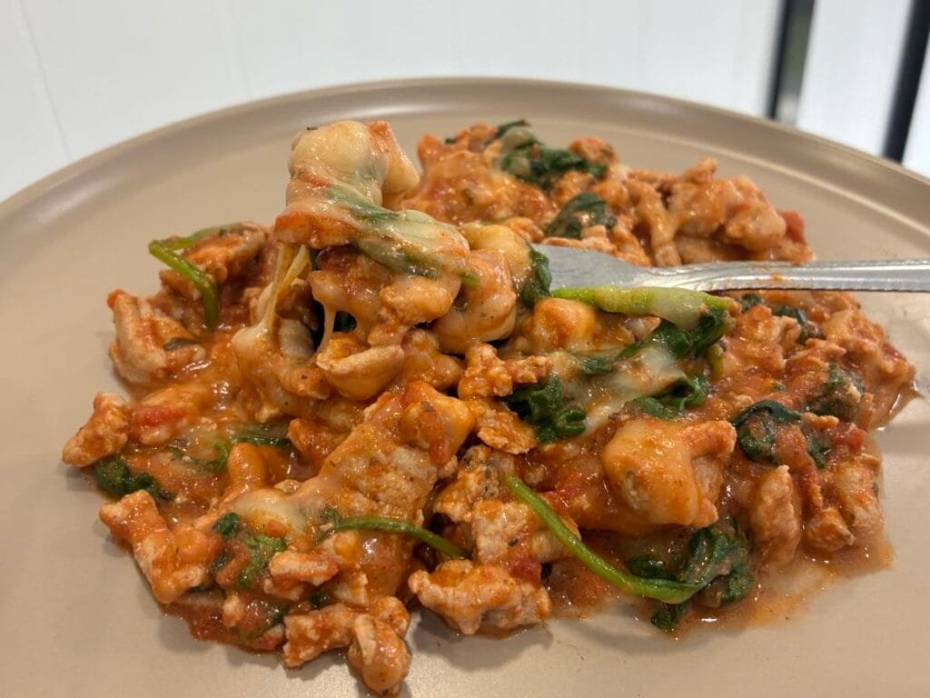 Side view of cheesy tomato garlic turkey melt on a plate with a stainless steel fork lifting a bite.
