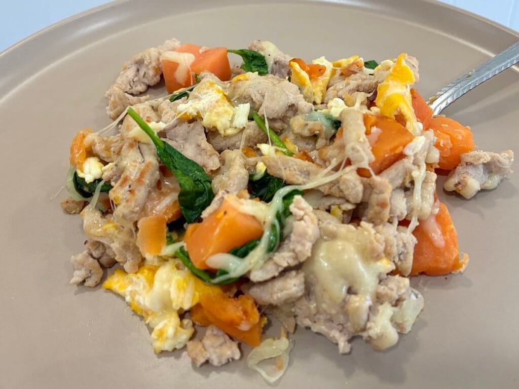 A hearty portion of turkey and sweet potato breakfast hash melt served on a clean plate, with a stainless steel fork resting in the cheesy egg scramble layers.
