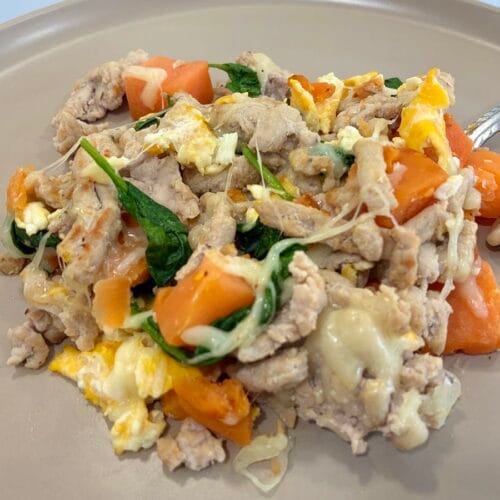 A hearty portion of turkey and sweet potato breakfast hash melt served on a clean plate, with a stainless steel fork resting in the cheesy egg scramble layers.