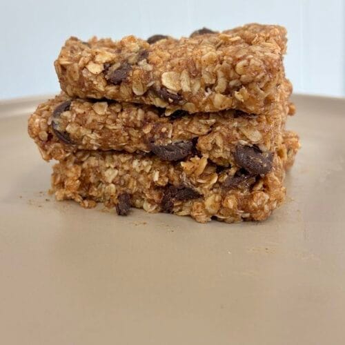Fudgy Almond Butter No-Bake Cookie Bars 5 Three thick, chewy squares of fudgy almond butter no-bake cookie bars stacked on top of each other on a matte stoneware plate, showcasing the dense oat and chocolate chip texture.