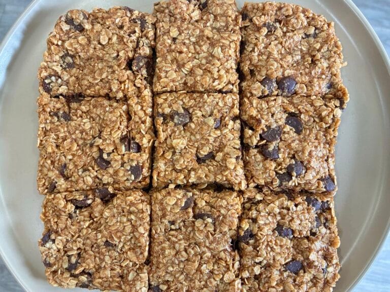 Fudgy Almond Butter No-Bake Cookie Bars 1 Top-down view of an uncut 8x8 pan of thick, fudgy almond butter no-bake cookie bars on a matte stoneware plate, showing a smooth nut butter surface packed with organic dark chocolate chips.