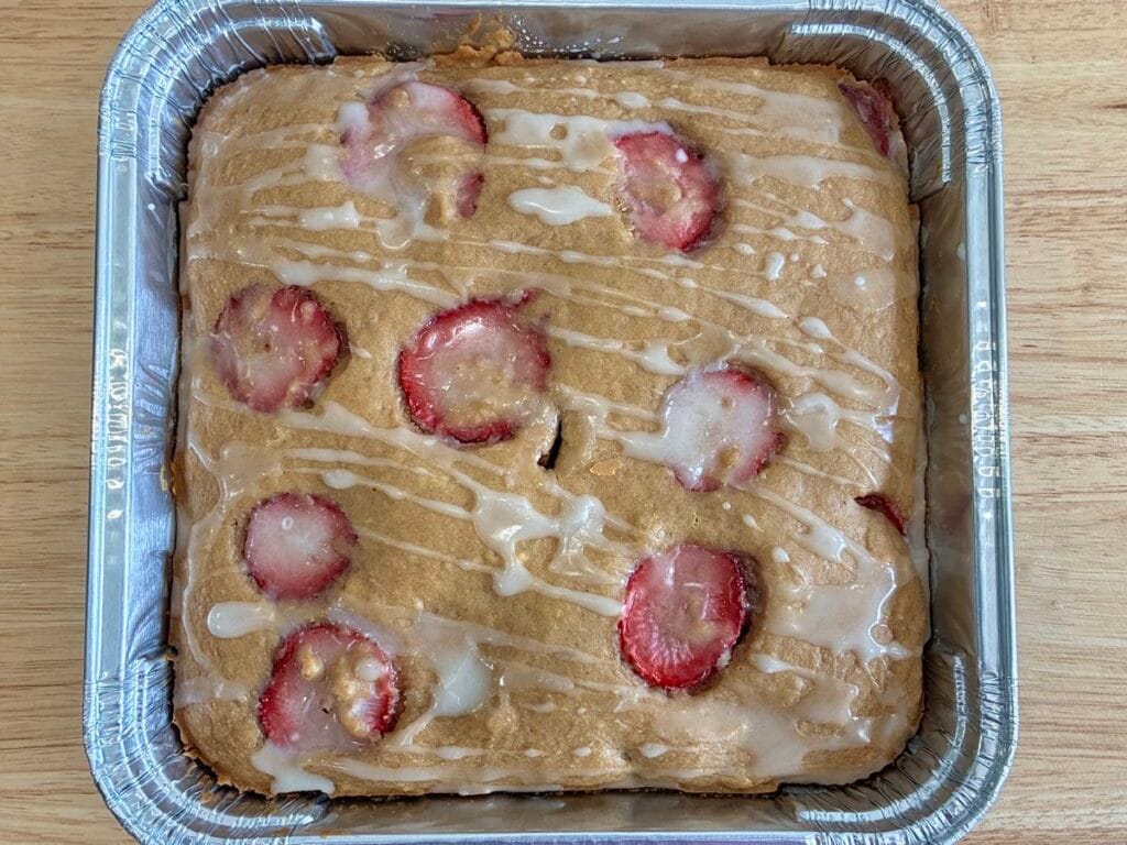 One-Bowl Strawberry Applesauce Snack Cake 2 A whole, uncut strawberry applesauce snack cake with lemon glaze inside a disposable foil baking pan.