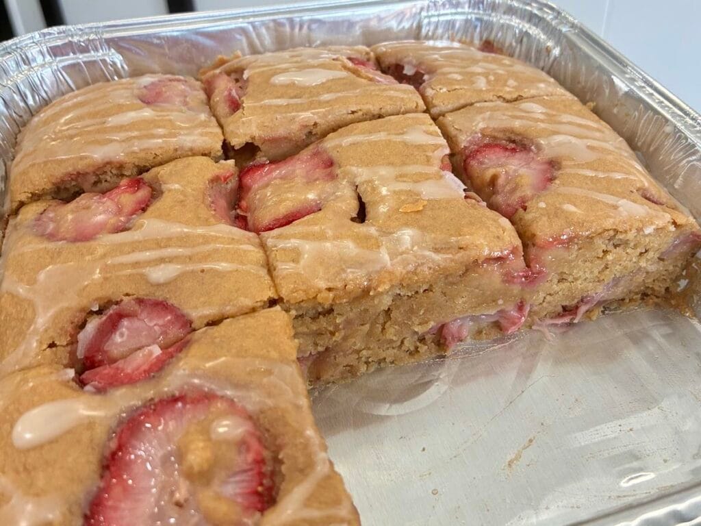 One-Bowl Strawberry Applesauce Snack Cake 3 Strawberry applesauce snack cake in a disposable foil baking pan with a couple of slices missing to reveal the interior crumb.
