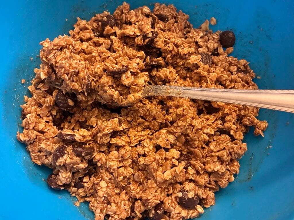 Fudgy Almond Butter No-Bake Cookie Bars 2 A large blue mixing bowl filled with raw, unrefined no-bake cookie dough made with creamy almond butter, pure maple syrup, quick-cooking oats, and folded dark chocolate chips.