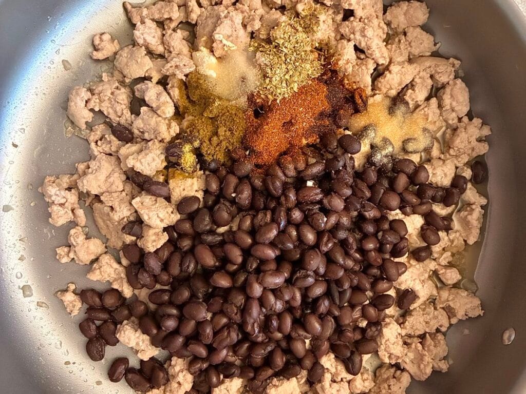 Raw seasoned ground turkey and black beans in a skillet pan before cooking