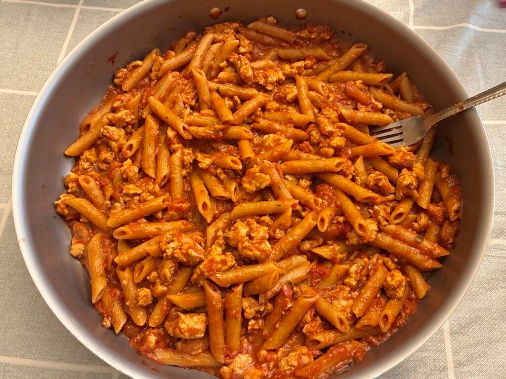 Pasta noodles simmering in a rich tomato and ground turkey sauce inside a large skillet.