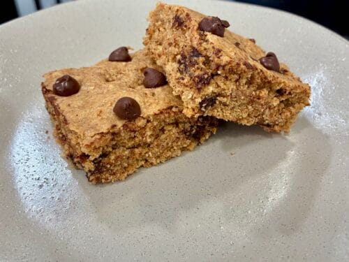 A plate of thick, fudgy almond butter oatmeal cookie bars showing melted chocolate chips.