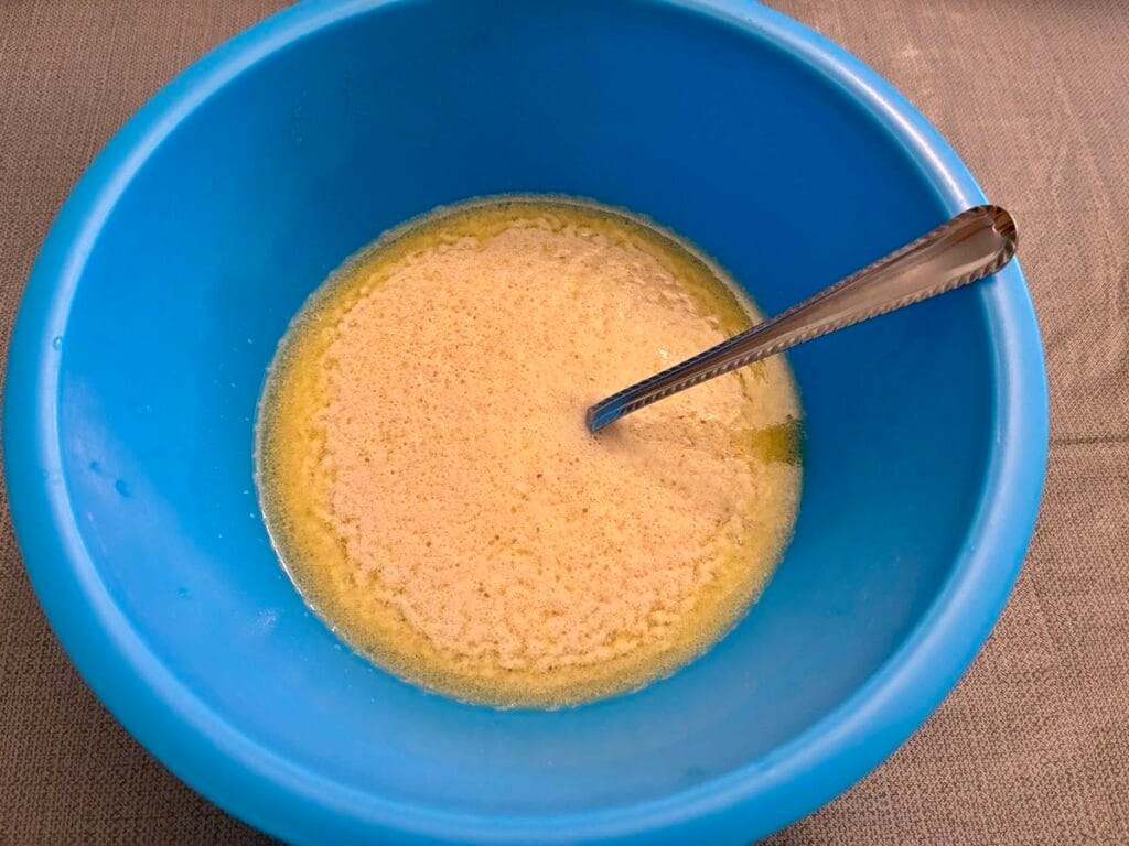 Activated yeast mixture foaming and bubbling beautifully inside a blue plastic mixing bowl.