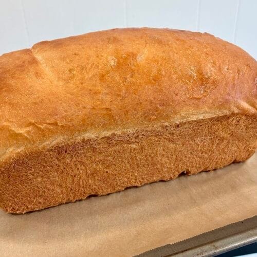 The Ultimate Easy Honey Butter Sandwich Bread (9x5 Pan Edition) 5 A whole loaf of homemade honey butter sandwich bread fresh from the oven, featuring a shiny, deep golden-brown crust on a baking sheet.