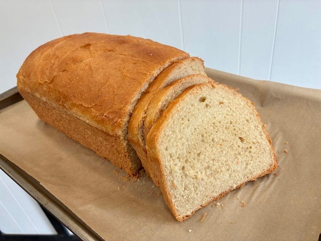 The Ultimate Easy Honey Butter Sandwich Bread (9x5 Pan Edition) 4 Thick, pillowy slices of homemade honey butter sandwich bread staggered neatly in front of the golden loaf on a cutting board.