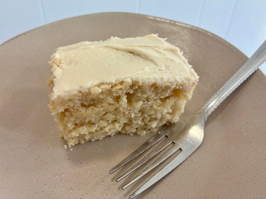 Easy One-Bowl Eggless Vanilla Almond Cake (8x8 Snack Cake) 2 A close-up view of a single square slice of moist vanilla almond snack cake on a plate with a dessert fork resting in front of it.