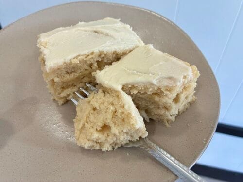 Square slices of moist vanilla almond snack cake cut cleanly and staggered on a dessert plate to showcase the soft interior crumb structure.