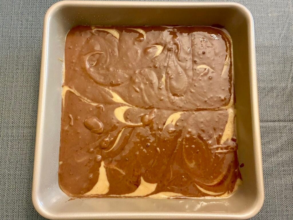 Vanilla and chocolate cake batter actively swirled together with a knife to create a marbled pattern before baking.