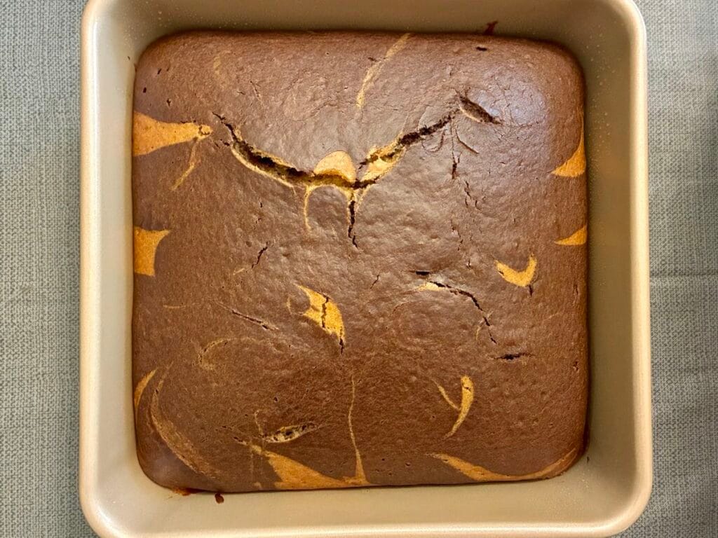 A freshly baked eggless marble snack cake straight from the oven, showing a golden brown surface with distinct chocolate swirls.
