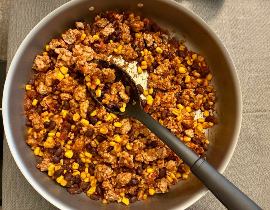 Ground turkey, black beans, taco seasoning, and sweet corn mixture cooking together in a large skillet before cheese is added.