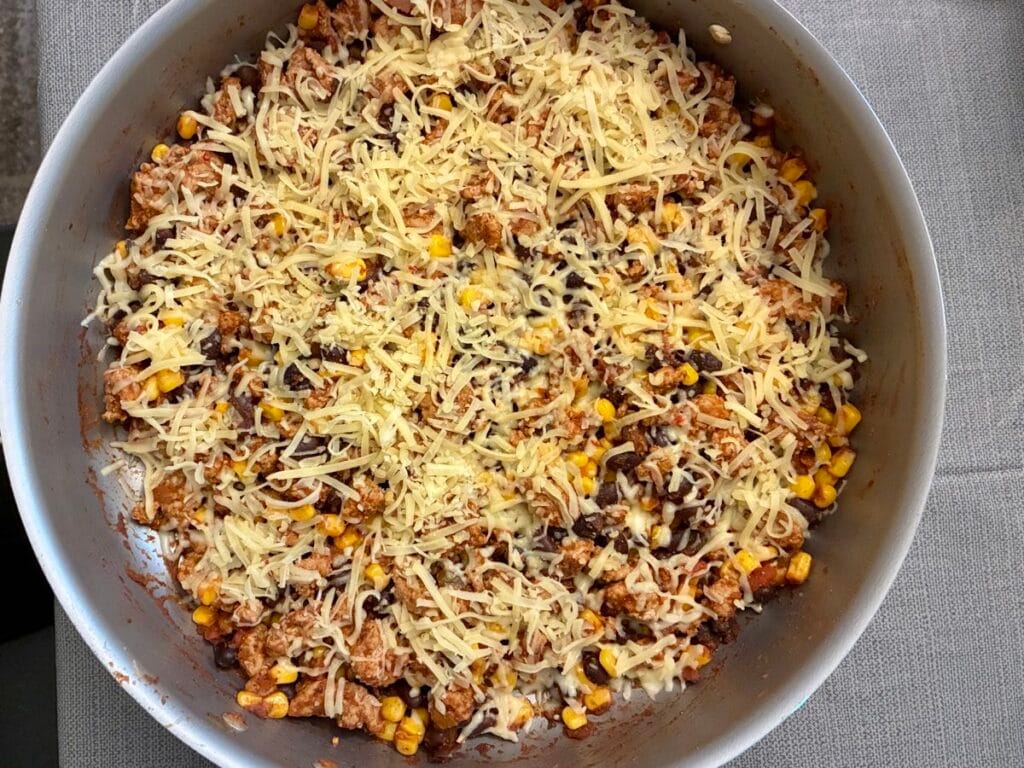 A layer of shredded Pepper Jack cheese freshly sprinkled over a hot ground turkey and black bean skillet meal.