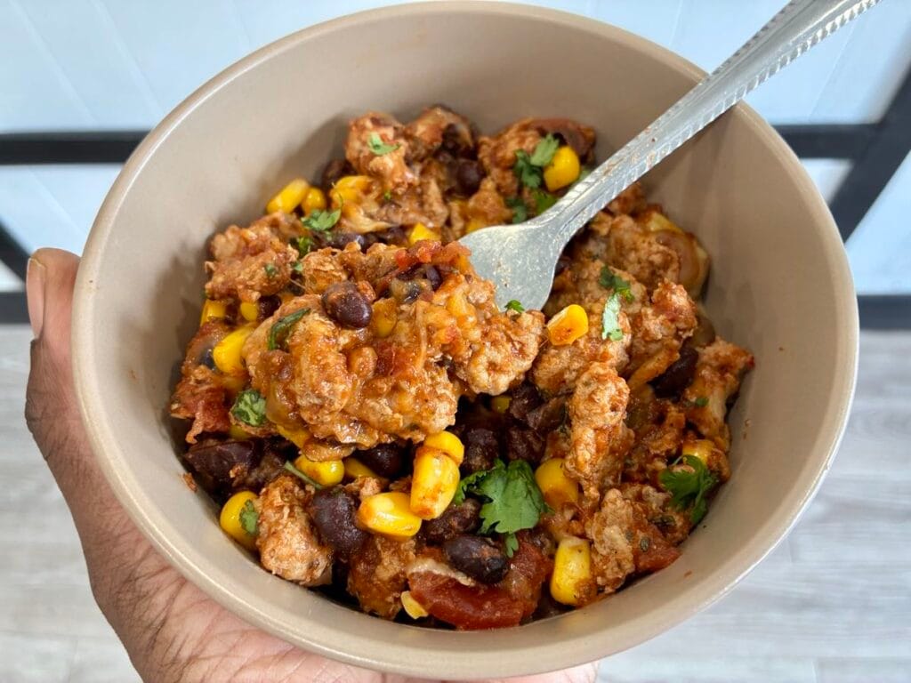 A dinner bowl filled with turkey taco skillet with a fork lifting up a bite of melted cheese and ground turkey.