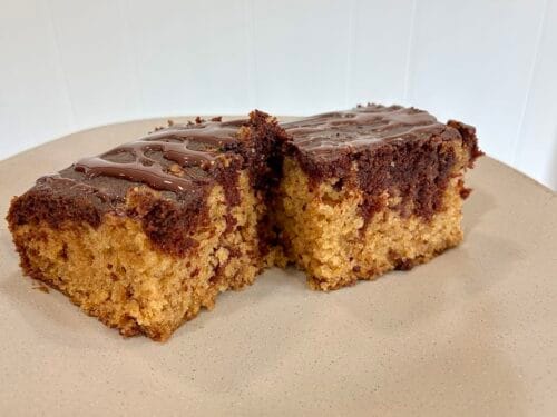 Two thick square slices of moist chocolate and vanilla eggless marble snack cake, topped with a chocolate glaze; served together on a clean dessert plate.