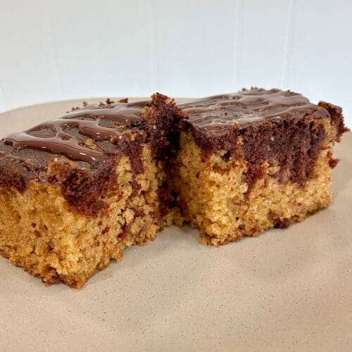 Two thick square slices of moist chocolate and vanilla eggless marble snack cake, topped with a chocolate glaze; served together on a clean dessert plate.