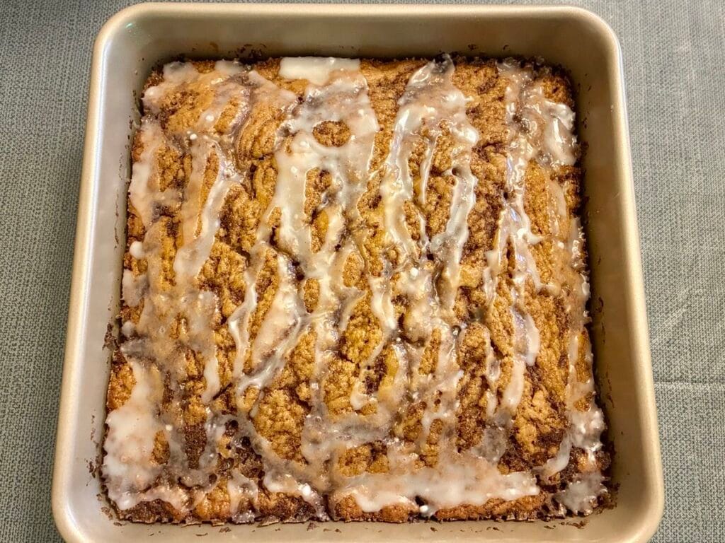 One-Bowl Cinnamon Swirl Snack Cake (Egg-Free Recipe) 4 A freshly baked cinnamon snack cake in a square pan topped with a glossy, sweet white powdered sugar glaze.
