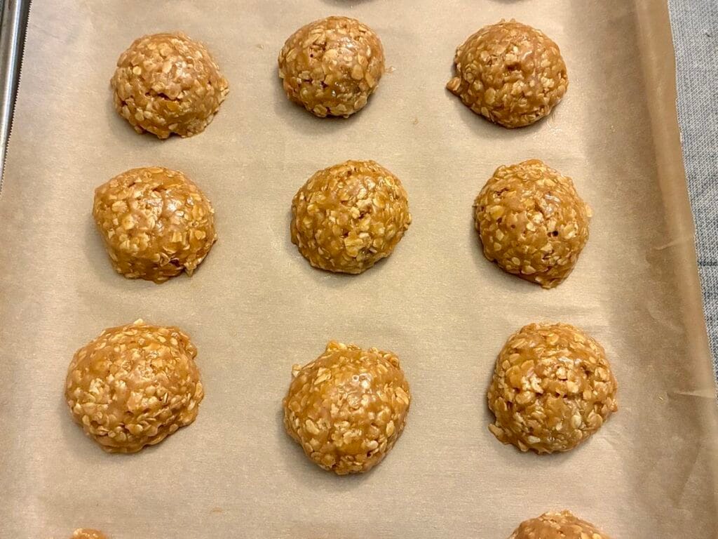 Raw scoops of oatmeal cookie dough made with golden coconut sugar arranged on a parchment-lined baking sheet before baking.