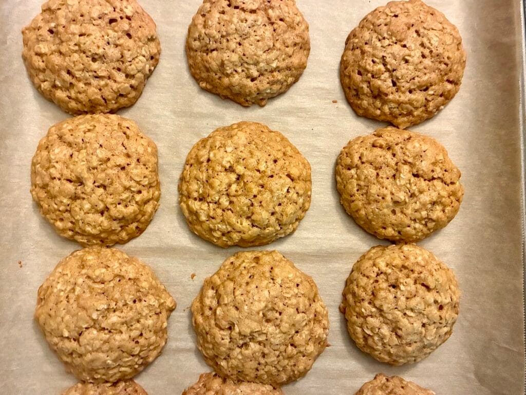 Golden brown oatmeal cookies fresh from the oven resting hot on a baking sheet, highlighting the thick and chewy texture.