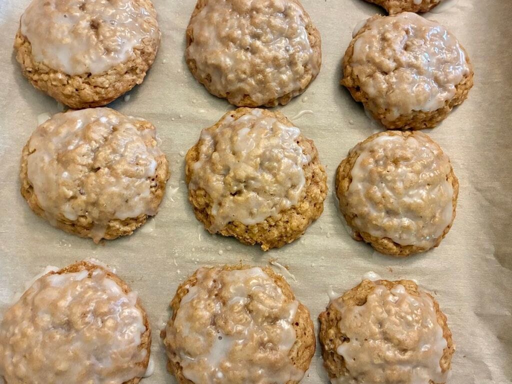 Thick homemade oatmeal cookies on a baking sheet topped with a smooth, sweet white icing drizzle glaze.