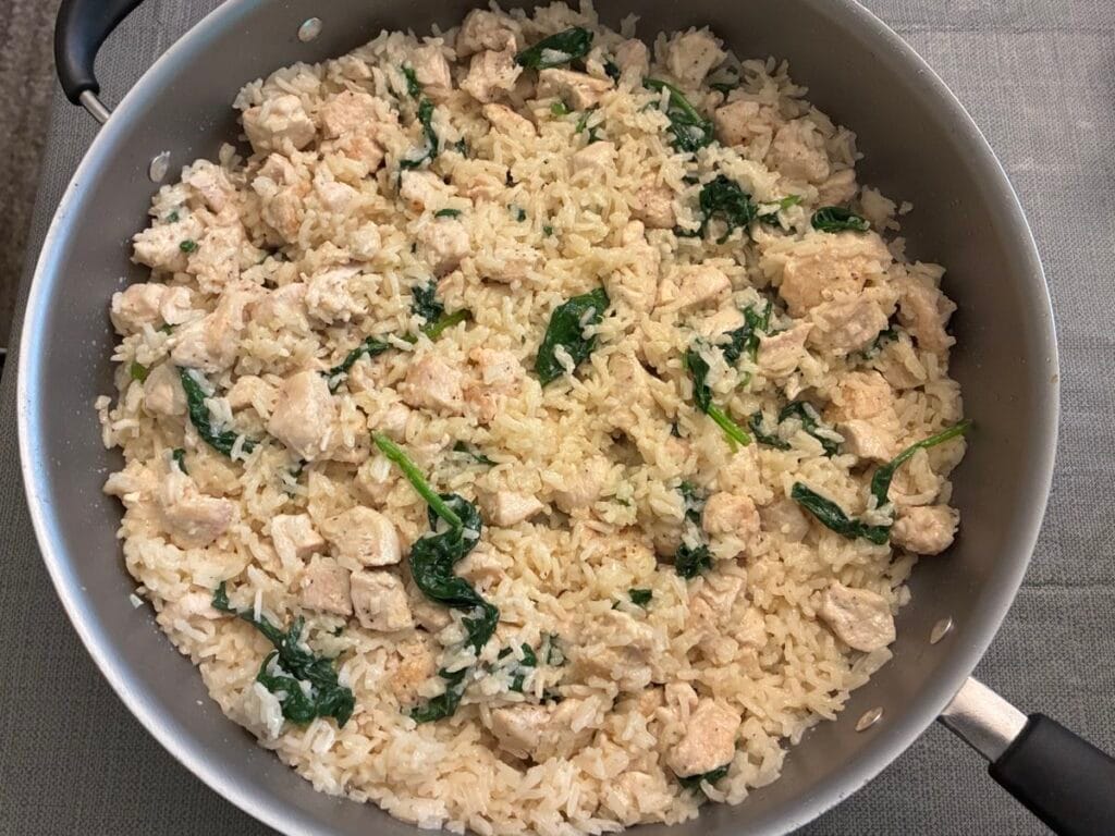 A single skillet filled with 20-minute one pan creamy garlic chicken and rice with wilted baby spinach fully incorporated.