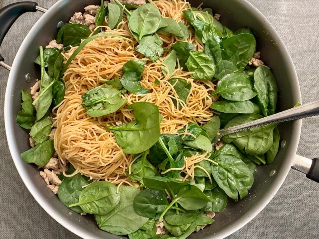 15-Minute Ground Turkey Garlic Noodles (Easy Asian-Inspired Recipe) 3 Fresh organic baby spinach leaves sitting in a skillet on top of spaghetti noodles.