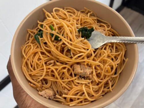 A unique close up shot of a fork twisting up a mouthful of glossy ground turkey garlic noodles from a serving bowl.