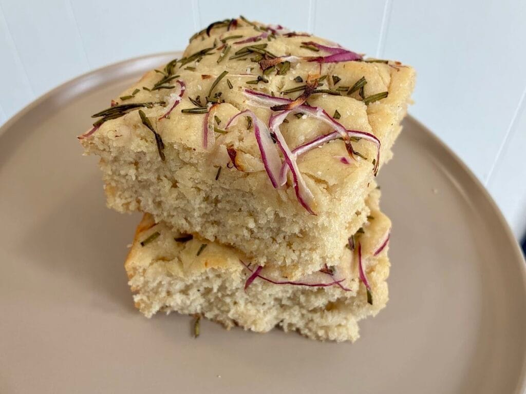Easy 8x8 No-Knead Focaccia (Beginner Friendly) 5 Slices of baked 8x8 no knead rosemary focaccia bread stacked to show the crispy crust and fluffy interior.