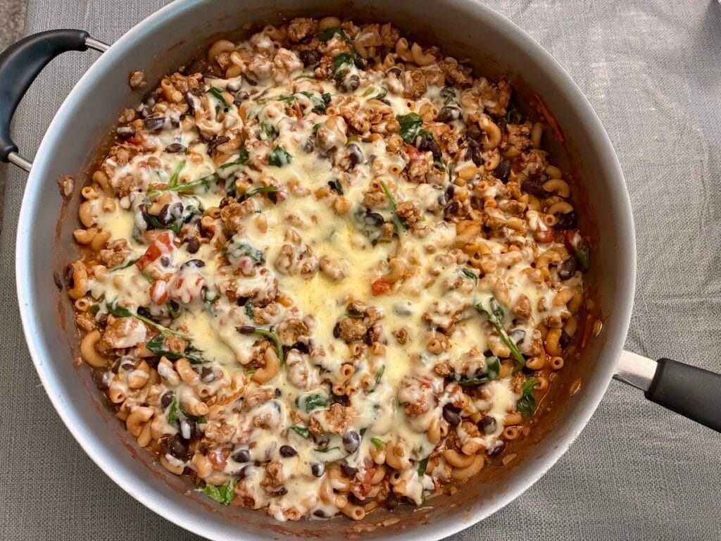 A deep skillet filled with completed turkey chili mac and pasta smothered under a thick layer of melted cheddar cheese.