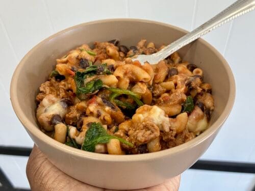 • A close-up shot of easy one-pot healthy chili mac skillet served in a matte stoneware bowl with a stainless steel fork resting in the pasta.