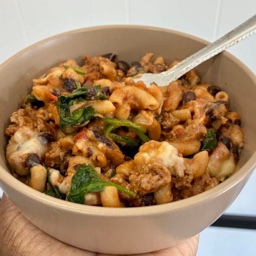 • A close-up shot of easy one-pot healthy chili mac skillet served in a matte stoneware bowl with a stainless steel fork resting in the pasta.