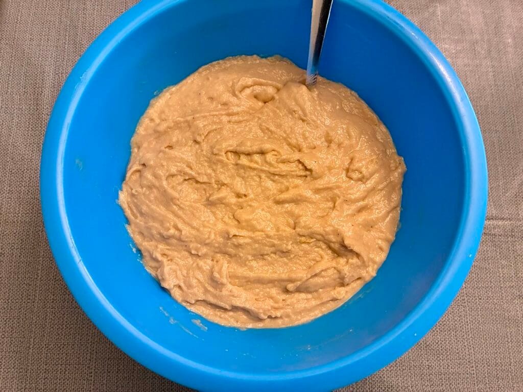 Thick golden-colored eggless cake batter combined inside a large blue mixing bowl.