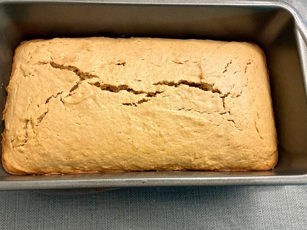 A freshly baked golden-brown lemon cardamom pound cake loaf sitting hot in the pan before cooling and glazing.