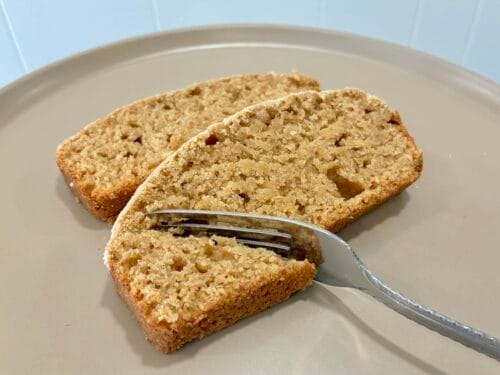 A close-up profile view of a couple of slightly staggered slices from an eggless healthy lemon cardamom loaf with a fork cutting into one piece.