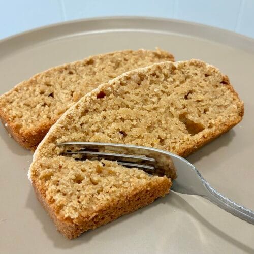 A close-up profile view of a couple of slightly staggered slices from an eggless healthy lemon cardamom loaf with a fork cutting into one piece.
