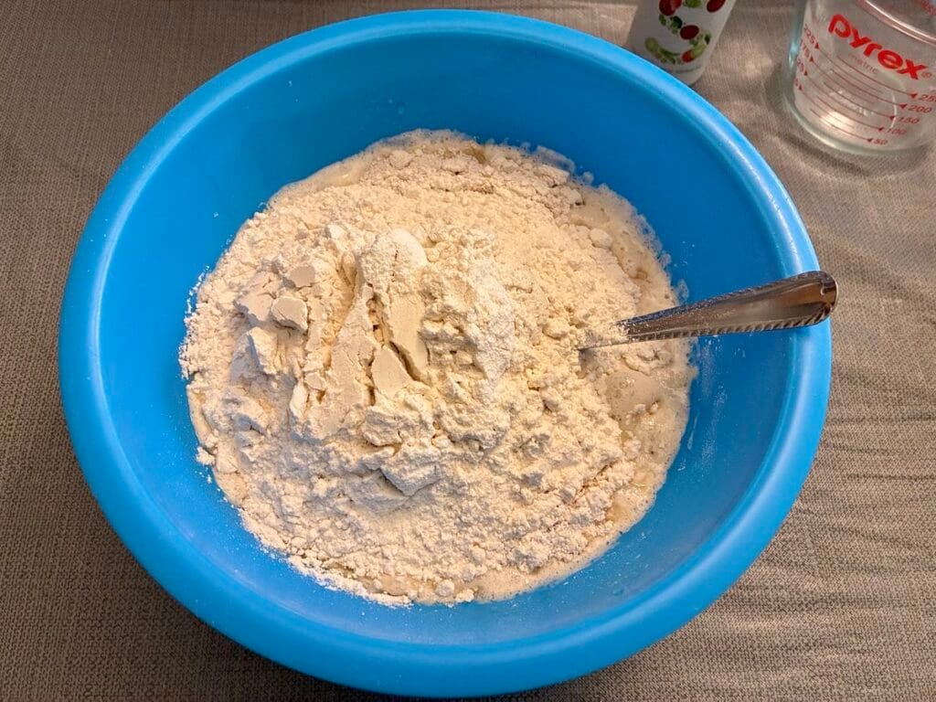 Healthy One-Bowl Artisan Pizza Dough (with An Oat Flour Twist) 3 Dry baking ingredients added on top of an activated yeast mixture inside a large blue mixing bowl.