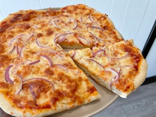 An angled view of a whole baked healthy one-bowl artisan pizza dough with a slice pulled out to showcase the texture of the oat flour crust, and toppings.