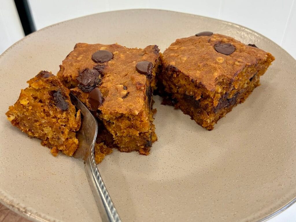 Healthy Eggless Pumpkin Chocolate Chip Snack Cake (8x8 Pan) 2 A close-up vertical food graphic showing a couple of slices of the moist eggless pumpkin chocolate chip snack cake on a small snack plate with a fork resting in one of the slices.